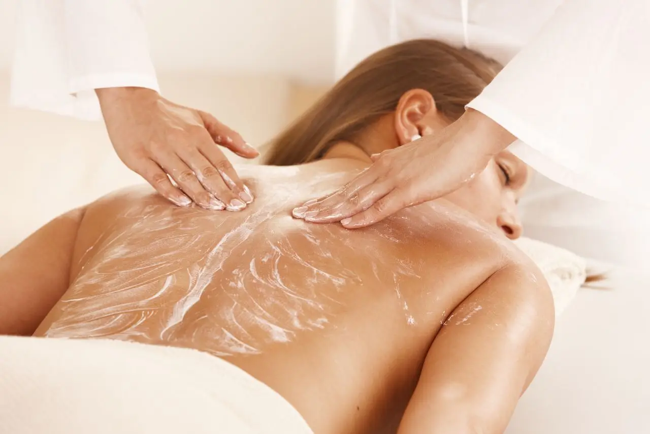Spa therapist applying cream on a woman’s back for a soothing massage in a clean and calm spa setting